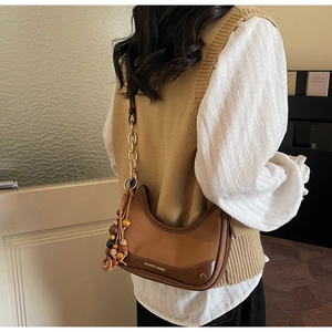 Brown half-moon dumpling bag with gold chain and colorful wooden bead charms on a model