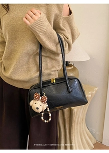 Detail of black vintage pillow bag with glossy leather texture and cute bear charm