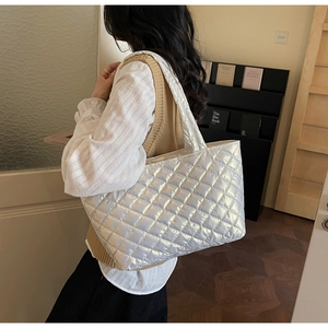 Silver quilted tote bag with metallic finish shown on shoulder in cozy interior