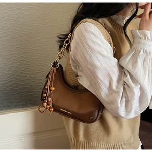 Brown leather moon bag detail with chunky metal chain and vintage beaded charm
