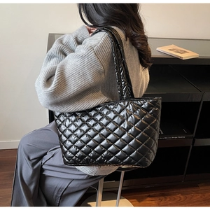 Detail of black quilted tote bag with shiny finish worn over a grey knit sweater