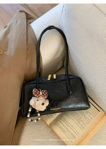 Detail of vintage black leather bag with bear charm on a cozy beige sofa
