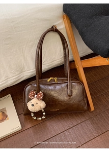 Detailed view of dark brown glossy Boston bag with plush bear charm on wood floor