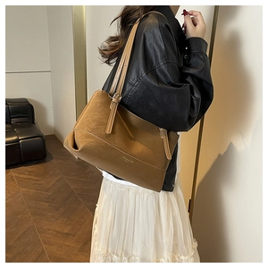 Detail of a large brown suede tote bag featuring adjustable leather straps and metal hardware
