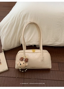 Macro detail of cream boston bag featuring pleated faux leather and teddy bear charm