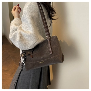 Detail of dark brown matte leather tote bag featuring gold lettering and adjustable straps