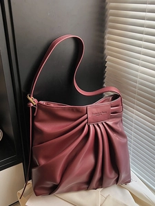 Burgundy pleated faux leather tote bag with adjustable strap in natural lighting
