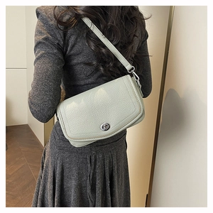 Detail of greyish-green lychee grain leather crossbody bag with silver turn-lock closure