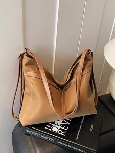 Minimalist brown retro leather tote bag with adjustable straps on a stylish book