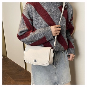 Close-up of off-white lychee leather crossbody bag with silver rotating lock on a model