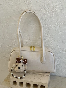 Retro cream white underarm pillow bag with plush bear charm on minimalist stone base