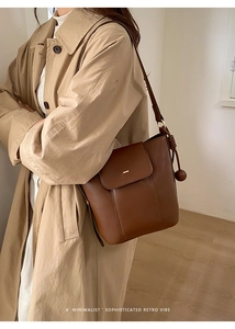 Detail of a brown leather bucket bag with a wooden bead charm and metal buckle