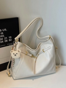 Minimalist white tote bag with gold hardware and plush bear charm for daily commuting