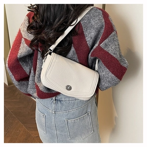 Detail of a creamy white litchi grain leather crossbody bag styled on a model's shoulder