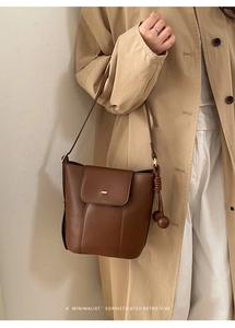 Detail of dark brown oil wax leather bucket bag with gold accents and knot pendant