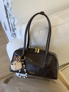 Vintage brown leather shoulder bag with bear pendant on a white sofa background