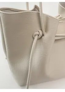 Close-up of drawstring knot detail on minimalist beige leather tote bag with fine texture