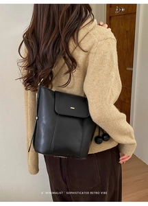 Rear view of model wearing minimalist black leather bucket bag with gold hardware detail