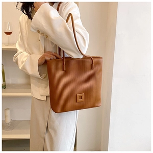 Detail of a brown pleated tote bag featuring vertical texture and slim shoulder straps