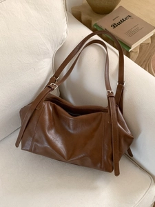 Vintage brown leather tote bag with adjustable straps on a soft white sofa