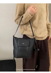 Detail of minimalist black leather bucket bag with gold hardware and spherical charm