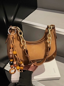 Retro brown crescent shoulder bag with gold chain and wooden bead charm on a book