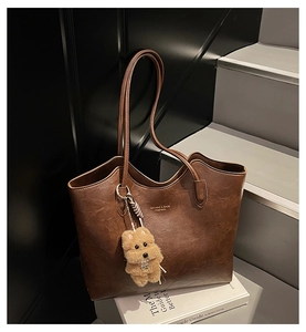 Brown vintage tote bag featuring long straps and a cute plush dog charm on white books