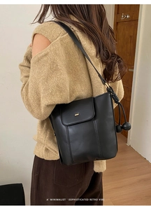 Close-up of black matte leather bucket bag with knot tassel detail on a female model
