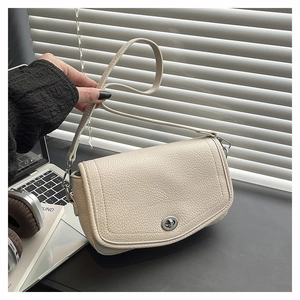 Close-up of beige lychee texture leather bag with silver metal twist lock on the desk