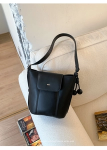 Detail of a black matte leather bucket bag with ball charms and magnetic flap closure