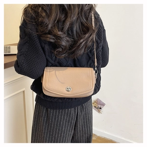 Gros plan du sac bandoulière en cuir beige avec fermoir rotatif argenté sur le mannequin