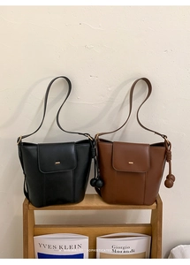 Minimalist leather bucket bags in black and caramel colors on a wooden shelf
