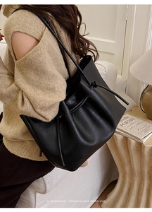 Rear view of a black matte leather drawstring tote bag worn on a shoulder in a cozy room