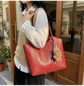 Detail view of red leather tote bag with gold logo and cute brown plush bear charm accessory