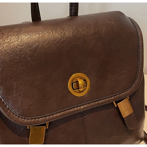 Detail of dark brown vintage backpack featuring glossy leather and gold metal twist lock