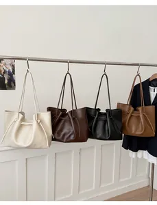 Row of large faux leather tote bags in cream, brown, and black with drawstring details