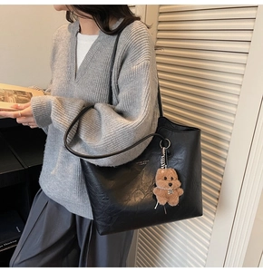Detail of black faux leather tote bag featuring a cute plush dog pendant and brand lettering