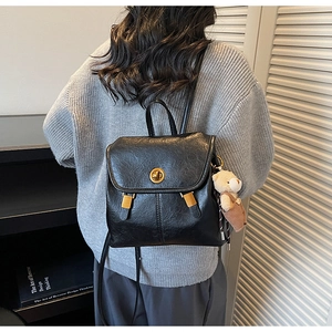 Close-up of vintage black faux leather backpack with gold clasp and plush bear charm