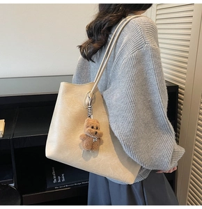 Close-up of beige leather tote bag featuring a cute brown teddy bear charm with pearls