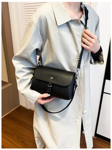 Detail of minimalist black crossbody bag with silver buckle worn on a gray coat