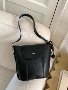 Minimalist black matte leather bucket bag with gold logo on a white textured sofa