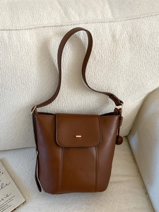 Minimalist dark brown matte leather bucket bag with gold buckle on textured sofa