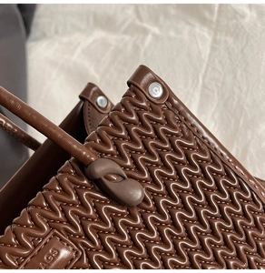 Detail of dark brown leather bucket bag with quilted waves and metallic rivet accents