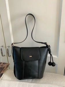 Minimalist black leather pumpkin bucket bag with round charm and adjustable shoulder strap