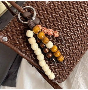 Detailed view of dark brown woven bucket bag with vintage wooden bead charm and silver hardware