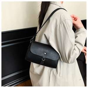 Close-up of minimalist black leather underarm bag with silver ring on beige trench coat