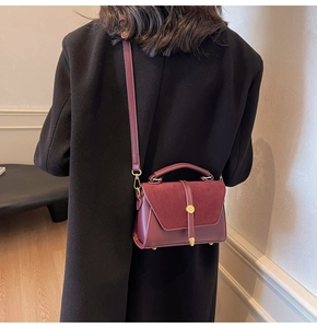 Detail of wine red crossbody bag featuring matte texture and gold buckle on a model