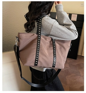Detail of a brown nylon tote bag with silver rivets and black leather trim for women