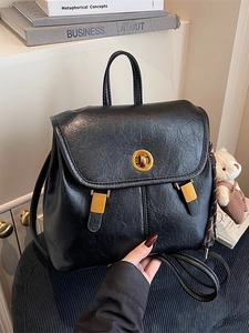 Vintage black faux leather backpack with gold metal lock and cute bear charm on a chair