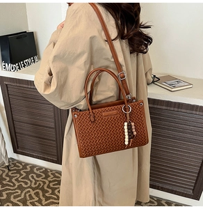 Close-up of brown woven leather bucket bag with tassels on a trench coat model